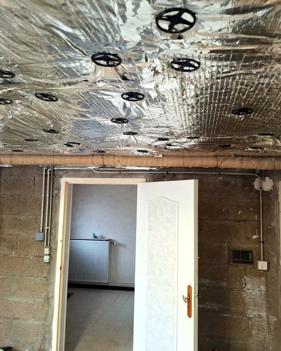 Plafond de sous-sol isolé avec panneaux à face aluminium, porte ouverte vers la maison – Galais Isolation, Ille-et-Vilaine