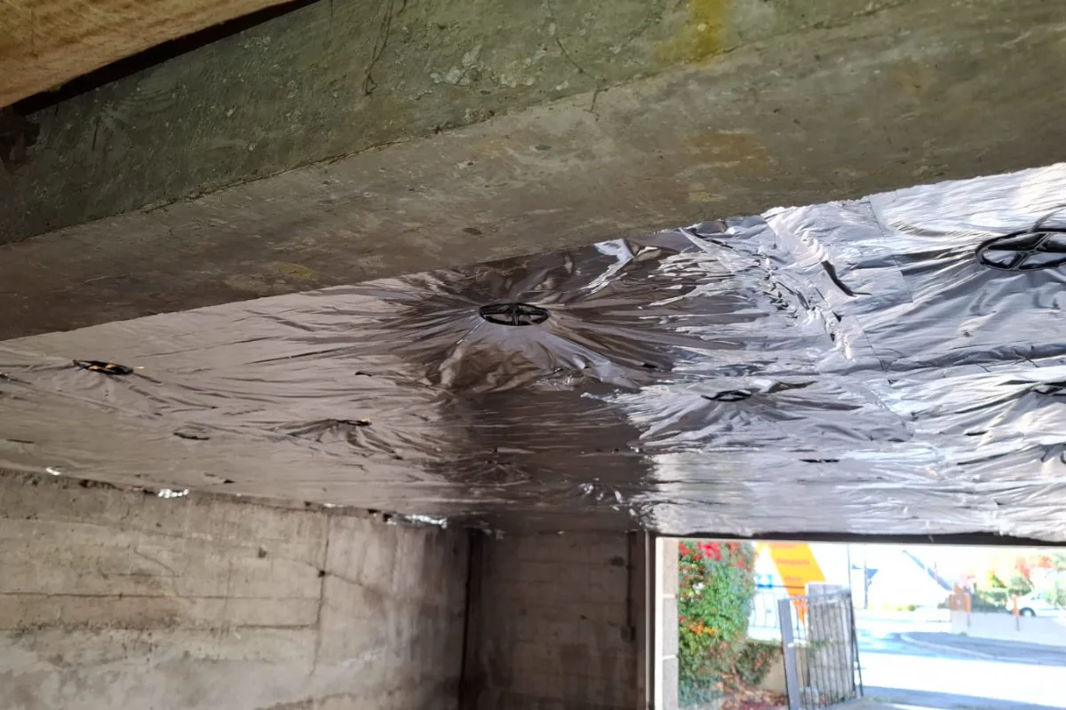 Panneaux isolants découpés et ajustés le long de la poutre au plafond du sous-sol à Martigné-Ferchaud (35)